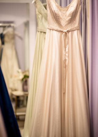 Formal gown hanging near a mirror in a softly lit fitting room with draped fabric in the background